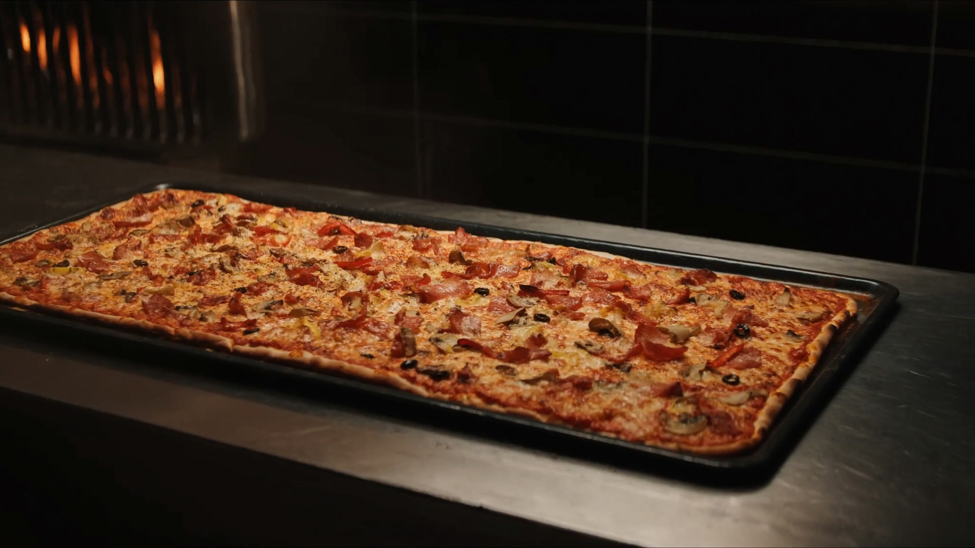Party-Pizza auf dem Blech, frisch aus dem Ofen auf dem Edelstahltresen