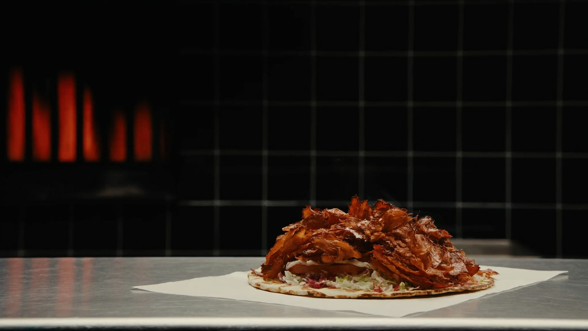 Frisch geschnittenes Drehspießfleisch auf Fladenbrot, dahinter der glühende Grill